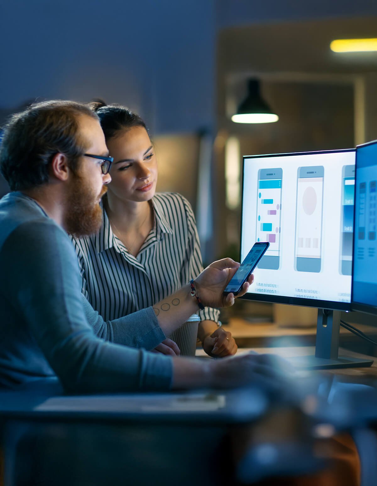 Dos personas analizan pantallas de una app móvil en un monitor mientras comparan elementos desde un teléfono.