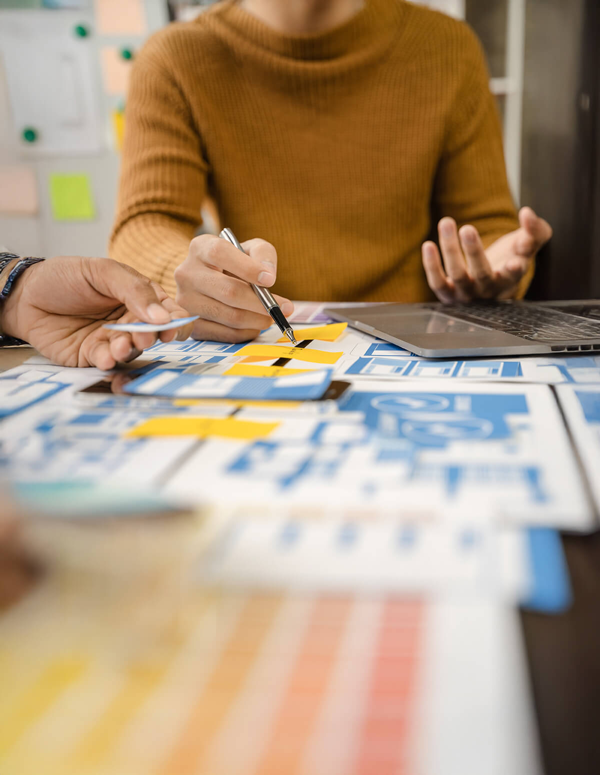 Personas revisando y organizando bocetos y diagramas de diseño sobre una mesa, trabajando en planificación visual y creación de proyectos.